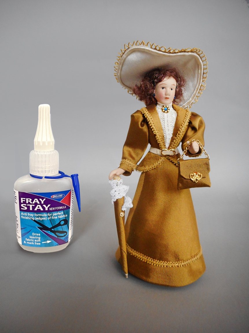 The finished 1/12-scale Edwardian lady doll in a gold silk gown, hat and parasol, beside the Fray Stay bottle